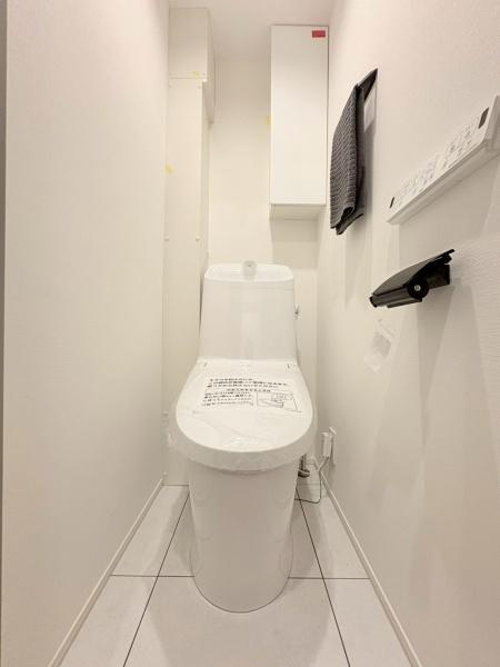 カサベルダのトイレ|白を基調としたシンプルなトイレ空間です。壁面収納や棚があり収納にも配慮されています。清潔感のあるデザインでお手入れもしやすい仕様です。温水洗浄機能付きの操作パネルも設置されています。