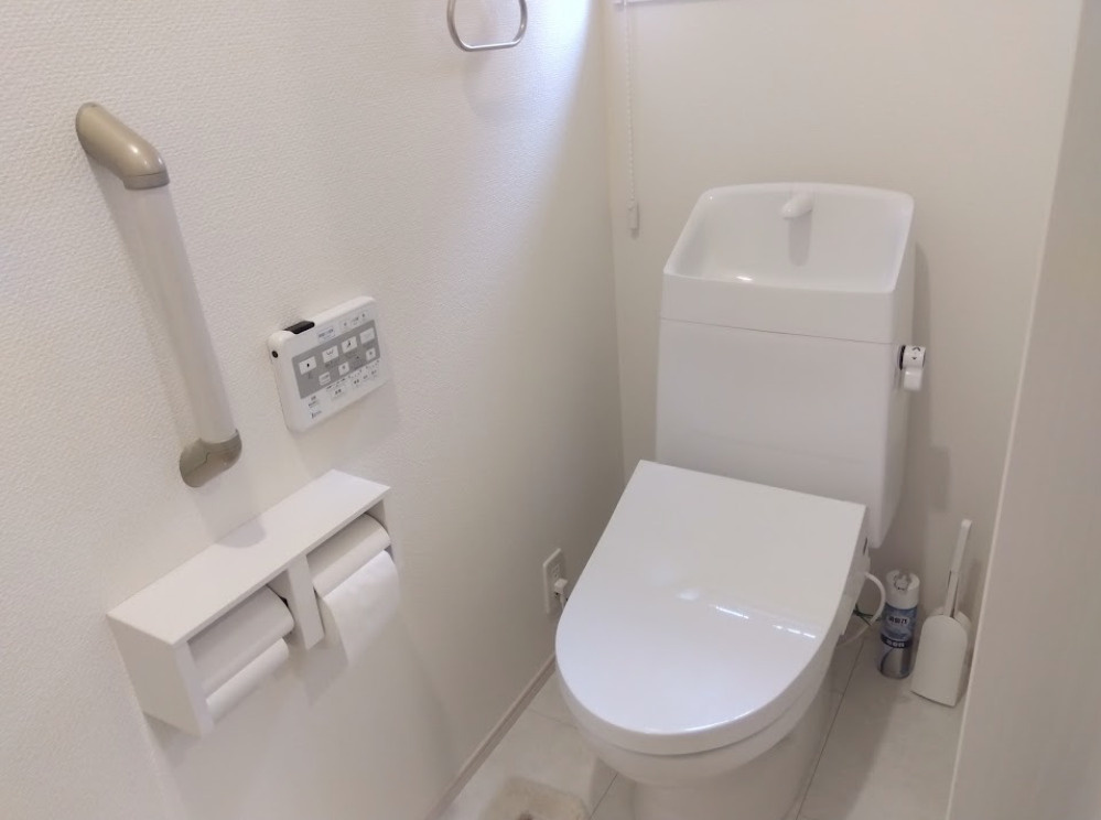 売中古戸建　三島市大場のトイレ|白を基調とした清潔感のある温水洗浄便座付きトイレです。壁面に便利なリモコンや手すり、２連式のペ－パ－ホルダ－を完備しています。どなたでも安心・快適に利用できる空間です。