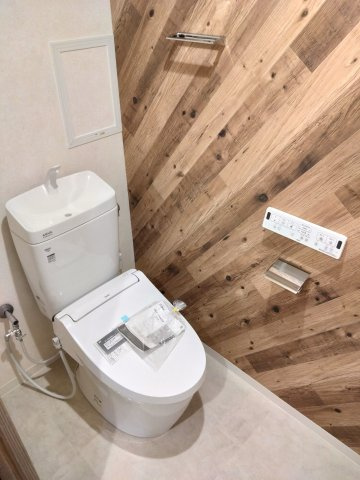 リバーガーデン森の城のトイレ|木目調のアクセントクロスが温もりを感じさせるトイレ空間。温水洗浄便座つきの洋式トイレは、手元で操作できる壁面リモコンで快適な使い心地です。