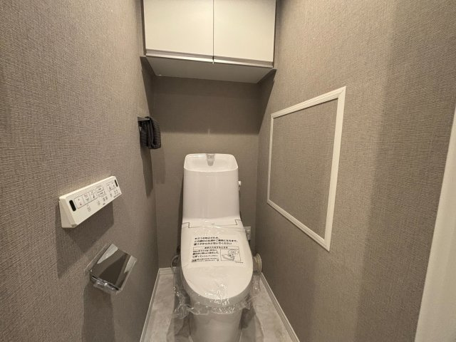 シティコープ西葛西のトイレ|落ち着いたグレージュ系クロスを採用した上質感のあるトイレ空間。吊戸棚を備えており、トイレットペーパーや掃除用品などをすっきり収納可能です。独立した空間設計のため、来客時も気兼ねなくご利用いただけます。