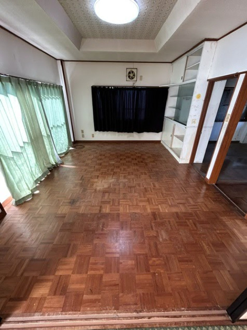 売中古戸建　三島市芙蓉台1丁目のその他|味わい深い寄せ木細工風の床と、開放的な折上げ天井が魅力のリビングです。大きな窓から光が差し込む広々とした空間で、壁面には便利な収納棚も備え付けられています。