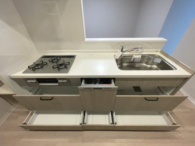 エメラルドマンション仁保新町のキッチン|床と親和性のある木目調のキッチンは、三口ガスコンロ、食洗乾燥機、スライドキャビネットと機能的です。
