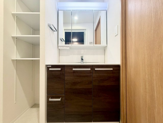 ハイマート弥刀の独立洗面台|ワイドな三面鏡付き洗面化粧台を採用。洗濯機置場の横には、タオルや洗剤を収納できる棚も備えています。