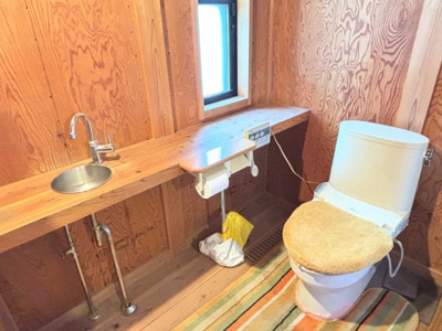 【トイレ】 | 中古一戸建　玉島阿賀崎三丁目　4LDK+S | 温水洗浄便座付きのトイレを1階に完備。手洗い器が独立して設置されており、衛生的に使えるのが嬉しいポイントです。天然木の壁と棚が、機能的ながらもこだわりを感じさせる空間に仕上げています。