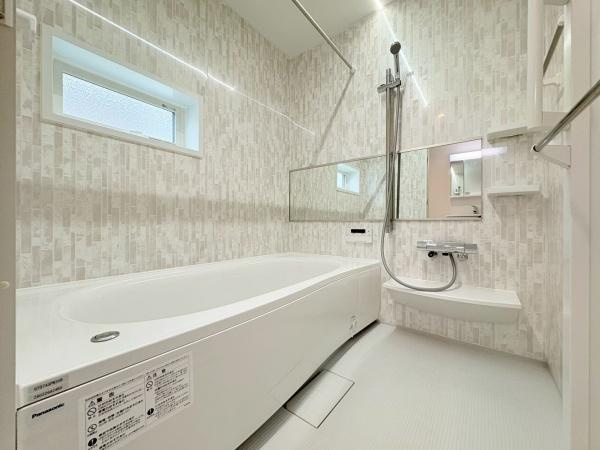 横浜市港北区鳥山町の新築一戸建の浴室|明るい採光窓がありバスルーム全体がすっきりとした印象です。大きめの浴槽でゆったりとした空間が広がります。スタイリッシュな壁デザインが魅力的です。使いやすく便利な収納棚も設置されています。