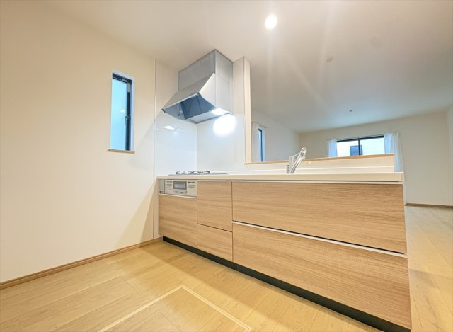 【キッチン】 | 富士見市水谷東1丁目　新築一戸建住宅　全4棟　(丸井志木店) | 木目調の面材がフローリングと調和するシステムキッチン。引き出し式の収納を備え、調理器具やキッチン用品も整理しやすい仕様です。グリル付きコンロで料理の幅も広がります。