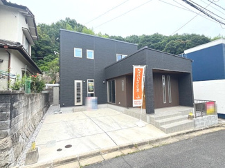 【外観】 | 佐伯区屋代3丁目（山陽女学園電停）【新築未入居】 | 南西側道路に面し、陽当りと通風に恵まれた配置設計。並列2台分のコンクリート敷き駐車場はフラットで、毎日のお車の出し入れもスムーズです。黒と木目調を組み合わせたスタイリッシュな外観が目を引きます。