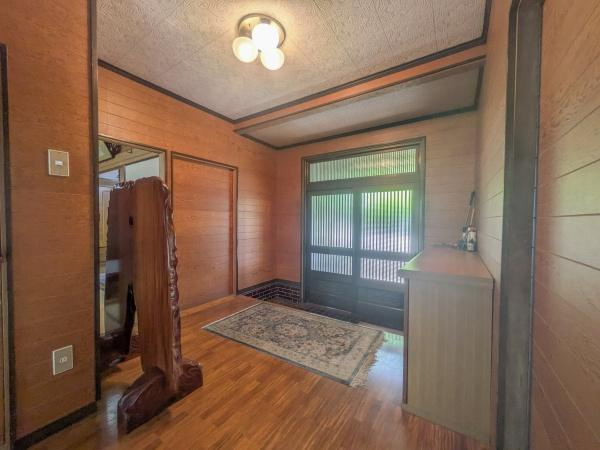 皆春　戸建ての玄関|木目調の壁と床が温かみを感じさせる玄関です。広々とした空間で収納も確保されています。大きな窓から自然光が入り明るい印象です。照明の配置も工夫されており落ち着いた雰囲気を演出しています。