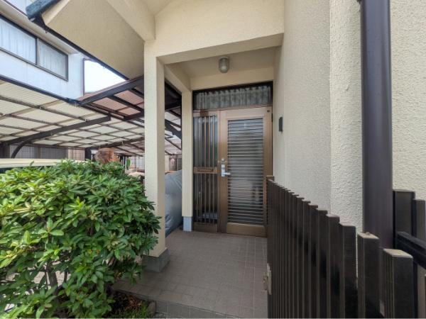 皆春　戸建ての玄関|玄関は屋根付きで雨の日も安心して出入りできます。植栽が彩りを添え落ち着いた外観が印象的です。明るい色合いの外壁とガラスを使用した扉が特徴です。段差が少なくアプローチがしやすい造りです。