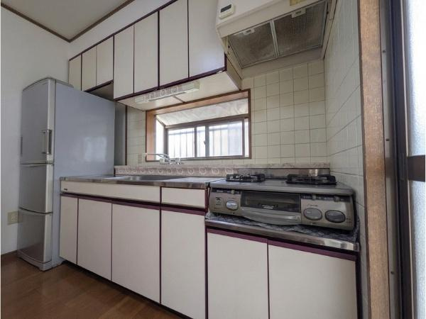 皆春　戸建てのキッチン|収納が豊富なキッチンです。ガスコンロと換気扇が設置されており調理しやすい環境が整っています。窓付きで明るい空間となっています。冷蔵庫スペースも確保されています。作業台も広めに設計されています。