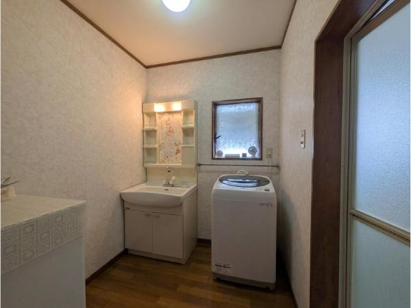 皆春　戸建ての独立洗面台|洗面台と洗濯機が並び使い勝手のよい配置です。収納棚付きの洗面台が実用的で整理しやすい印象です。窓があり自然な明るさが差し込みやすい空間になっています。全体的にスッキリとしたレイアウトです。