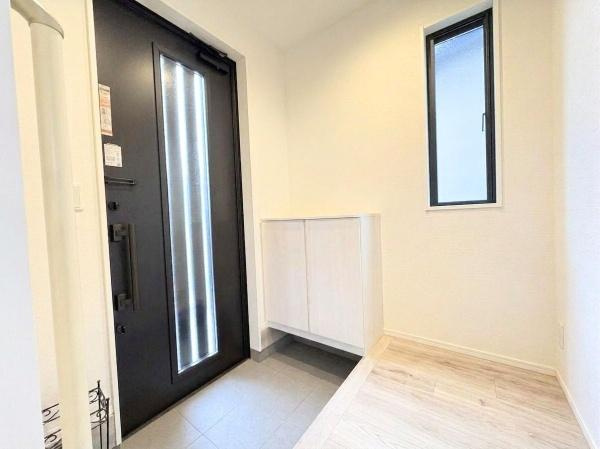 丹生　戸建ての玄関|大きな窓からの自然光が広がり収納スペースも設けられています。シンプルなデザインでさまざまなインテリアに合わせやすい印象です。床の切り替えが特徴的なアクセントとなっています。