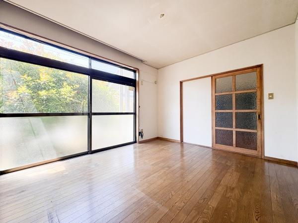 富士見が丘西4丁目中古の洋室|大きな窓から豊かな自然光が降り注ぐ洋室です。落ち着いた色合いのフローリングが特徴的です。シンプルな壁面とガラス扉が開放感を演出します。
