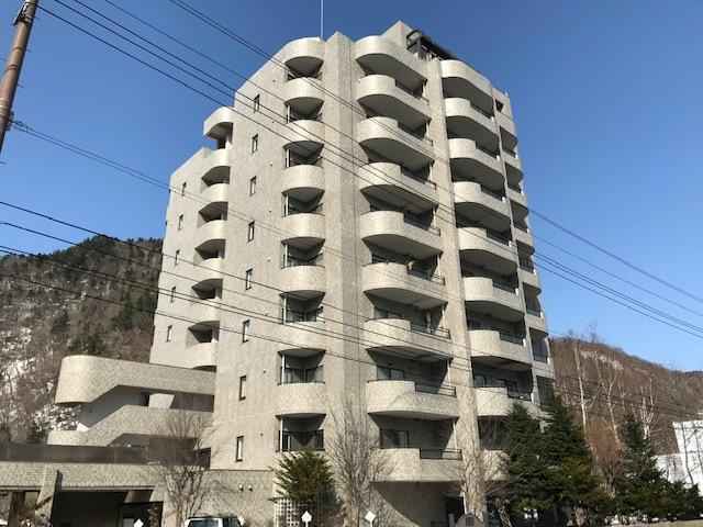 豊かな自然に囲まれた、グレーのタイル貼りと丸みのあるバルコニーが印象的な10階建マンション。