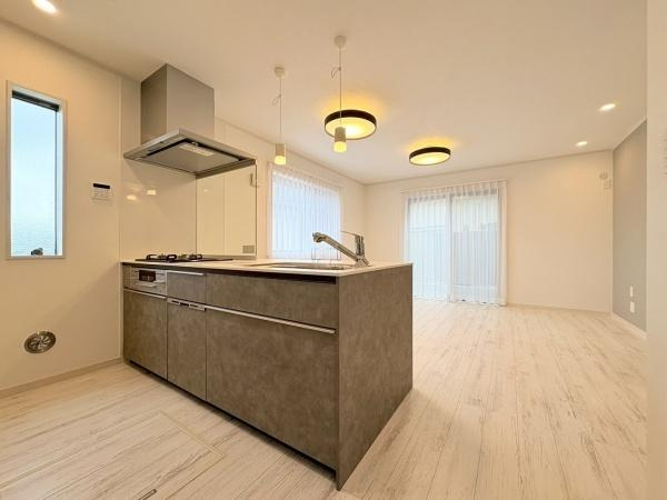 横浜市旭区川井本町の中古一戸建のキッチン|シンプルで洗練されたキッチンが印象的です。対面式で開放感があります。高い天井と大きな窓から光が差し込み明るさを感じます。床や壁の色合いが落ち着いた雰囲気を演出しています。照明もおしゃれなデザインです。