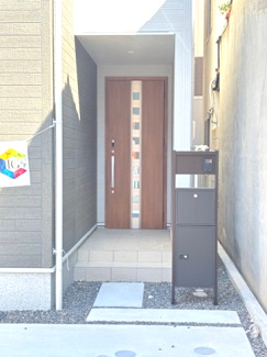 【玄関】 | 西区東観音町（全3区画）3号棟　 | 木目調の玄関ドアが温かみを添えるエントランス。不在時に重宝する宅配ボックス付きの機能門柱を設置しており、再配達の手間を省けます。屋根のあるポーチ設計で、雨の日の出入りも安心です。
