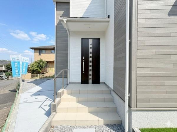 横浜市旭区金が谷２丁目の新築一戸建の玄関|モダンなデザインが目を引く玄関です。明るいタイルが清潔感を与えています。手すりが備え付けられており安心です。外壁とのコントラストも印象的です。開放感のあるアプローチが魅力です。