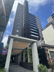 【外観】 | コンクリート打ちっぱなしと木目調のルーバーが調和した、モダンなエントランスアプローチ。植栽の緑が優しく迎え、住まうことへの誇りを感じさせます。オートロック完備で、セキュリティ面も安心です。