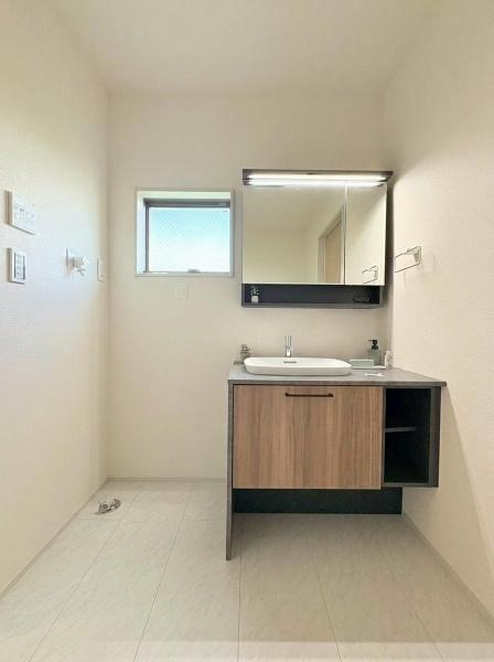 大和市福田の新築一戸建の独立洗面台|鏡付きの洗面台と収納が設けられています。ホワイトをメインにした空間にシックな色で統一された洗面台のデザインです。洗濯機置き場もあり使い勝手が良い印象です。