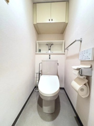 【トイレ】 | 白を基調とした清潔感あふれるトイレ空間。限られたスペースながらも、吊戸棚などの収納があり、ペーパーや掃除用具をすっきりと隠せます。毎日使う場所だからこそ、衛生的で落ち着ける仕様です。
