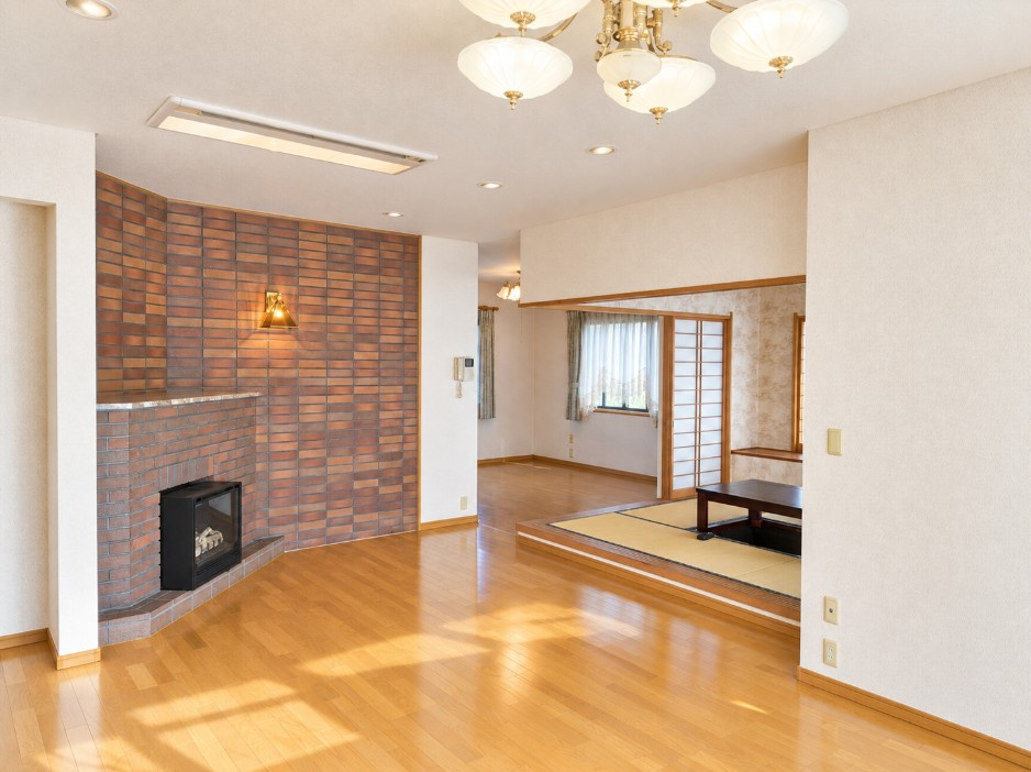 東松山市五領町中古戸建の居間・リビング|広々としたフローリングと和室がつながる開放的な空間。暖炉風の設備が落ち着いた雰囲気を演出します。