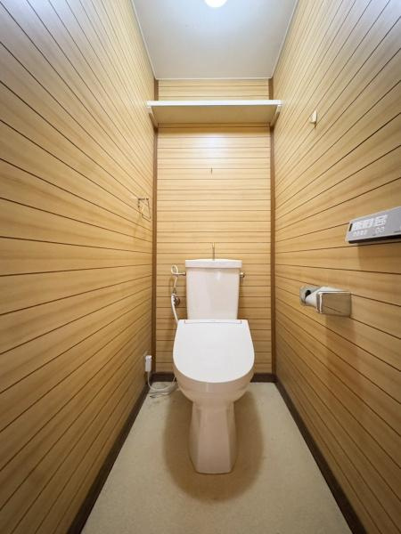 エメラルドマンション古国府のトイレ|木目調の壁面が特徴的なトイレです。室内はシンプルで手入れがしやすい空間。上部には便利な棚が設置されています。照明の明るさも十分に感じられる仕様です。