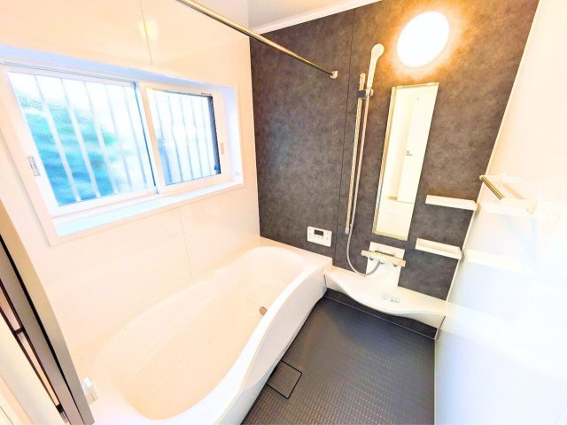 松山市越智２丁目の中古一戸建の浴室|窓付きのバスルーム。ミラー横に小物棚と手すりを備えたユニット仕様