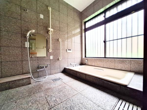 大字寒田　戸建ての浴室|広々としたバスルームは石造りの壁と床が落ち着いた雰囲気を演出します。大きな窓からは自然光がたっぷり差し込み空間全体が明るく感じられます。