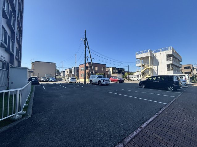 【駐車場】青空の下、アスファルトが敷かれた広々とした屋外駐車場。