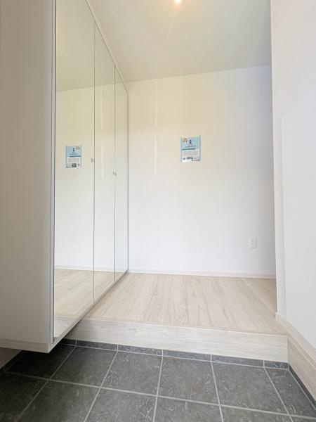 大和市上和田の新築一戸建の玄関|ホワイトカラーをメインに、シックな扉で落ち着いた雰囲気に。全身鏡でみだしなみチェックもでき、鏡を開くと収納可能な棚があります。
