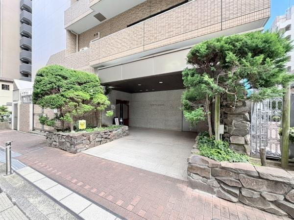 ベイサイトコート横浜のエントランス|石造りのアプローチと緑豊かな植栽が落ち着いた雰囲気のエントランスを演出しています。建物の外観はすっきりとしたデザインで印象的です。エントランス前は広々としておりゆとりを感じられます。