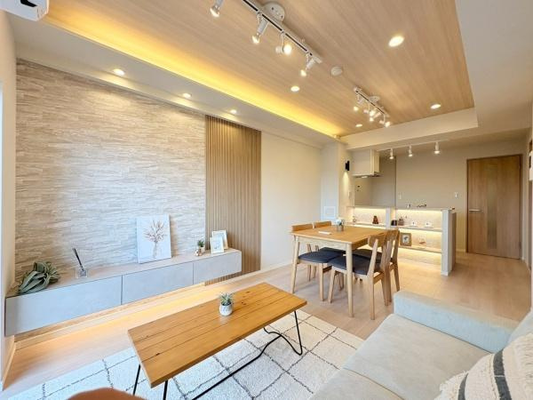 ベイサイトコート横浜の居間・リビング|ナチュラルな木目天井と間接照明が空間に落ち着いた雰囲気を与えています。リビングの壁面にはデザイン性のある石目調が施されアクセントになっています。床や家具の色合いも統一されており室内が広く感じられます。