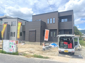 【外観】 | 令和8年7月完成予定、建築中の現地外観写真です。スクエアを基調としたモダンなフォルムと、落ち着いたトーンの外壁が周囲の街並みに映える、並列3台駐車可能なゆとりある敷地です。