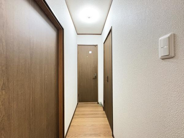 政所　中古の内装|廊下には落ち着いた木目調のドアが並びシンプルで清潔感のある空間です。天井の照明が明るさをしっかりと確保し壁はホワイトで統一されています。左右に複数のドアがあり各部屋へのアクセスも便利です。