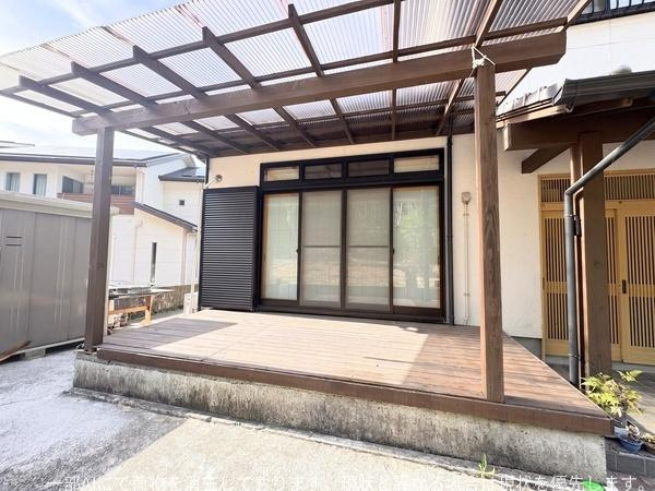 政所　中古のその他|広々としたウッドデッキが設置されています。屋根付きなので天候による影響も少ないです。サッシ窓があり室内との行き来が便利です。周囲に生活感のある住宅街が広がっています。