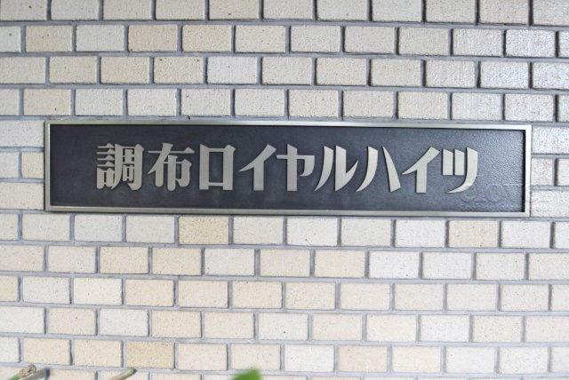 【現況写真】 | 調布ロイヤルハイツ | エントランスに掲げられた、マンション名を示す館銘板。さほど激しく主張はしませんが、しっかりと掲示されています。～即日のご見学可能～　お問合せはお気軽にどうぞ。