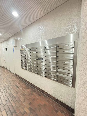 クローバーハイツ三宮の設備|【集合ポスト】一階共用部に設置されたダイヤル式の集合ポストです。ステンレス製のユニットが壁面に並んでいます。