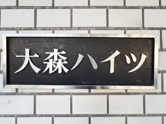 【現況写真】 | 大森ハイツ | エントランスに掲げられた、マンション名を示す館銘板。さほど激しく主張はしませんが、しっかりと掲示されています。～即日のご見学可能～　お問合せはお気軽にどうぞ。
