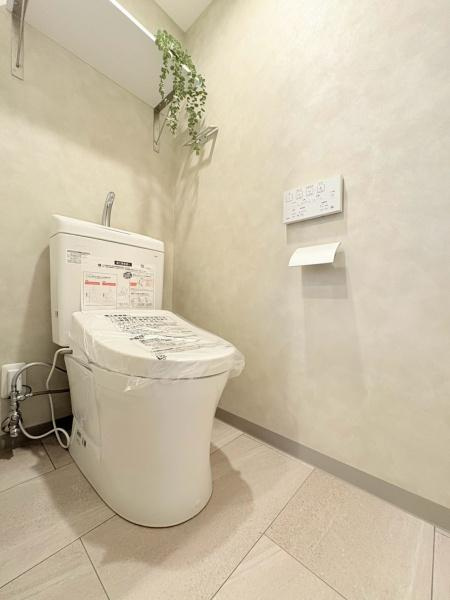 六会駅前高層住宅のトイレ|明るく清潔感のあるトイレです。壁付けの操作パネルが設置され使い勝手に配慮されています。収納棚も備わっておりシンプルですっきりとした空間です。床面は落ち着いた色合いでお手入れも簡単です。