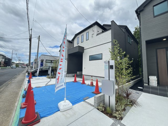 八王子市四谷町2期の前面道路含む現地写真|右側から見た外観写真です。こちらの角度からも建物の立体感をご確認いただけます。手前には広い駐車スペースを確保しております。青空に映える明るい外観で、毎日を気持ちよく過ごせそうです。