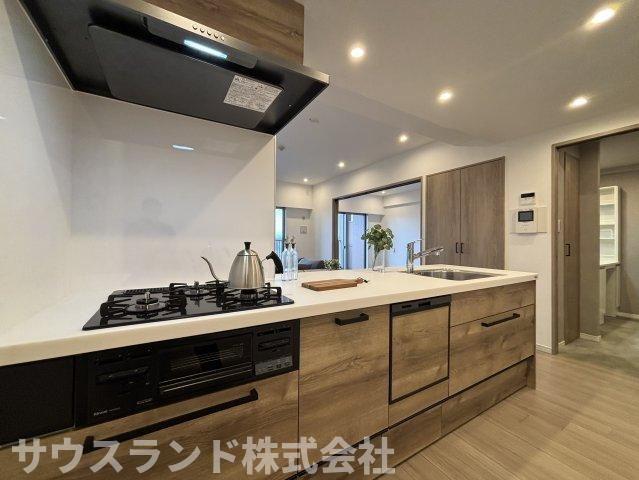 マクシスタワーズアーバンデュオのキッチン|木目調の面材が印象的な対面キッチン。調理スペースを確保しながら、リビング側とのつながりも感じやすい配置です。収納や設備もまとまりよく、毎日の家事を進めやすい空間に仕上がっています。