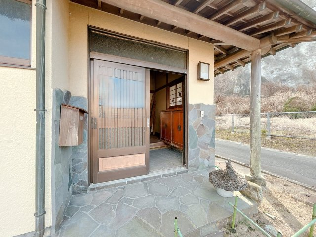 いわき市四倉町鬼越中古住宅 4LDK 陽当たり良好 三面角地！ 不動産プラスの玄関|【リフォーム中】外から見た玄関の写真です。しっかり軒が出ているので雨の日でも濡れることなく出入りできますね。玄関は新品交換いたします。石の腰壁部分もサイディングに張り替えます。