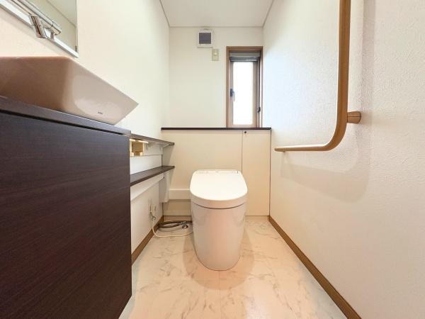 三芳　中古のトイレ|白を基調とした明るい空間が印象的なトイレです。手すりが設置されており使い勝手にも配慮されています。窓があるため自然光を取り入れることができます。収納スペースも備わっています。