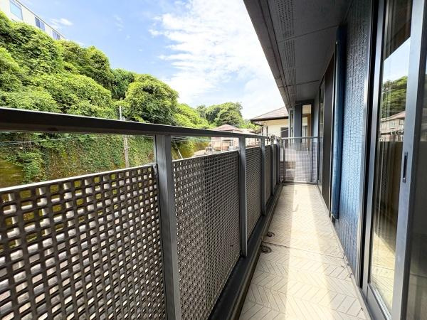 三芳　中古のバルコニー|奥行きのあるバルコニーが広がっており複数の窓から光が入ります。周囲には豊かな緑が広がり開放感を感じられます。金属素材の手すりで視界が確保されています。床面にはデザイン性のある素材が使用されています。