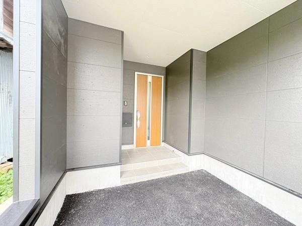 藤沢市城南２丁目の新築一戸建の玄関|玄関まわりがゆったりとした印象です。外壁と調和したデザインの玄関ドアが特徴的です。雨天時も安心な屋根のあるアプローチです。玄関ポーチは清潔感のある仕上がりです。段差が少なく出入りしやすい設計です。