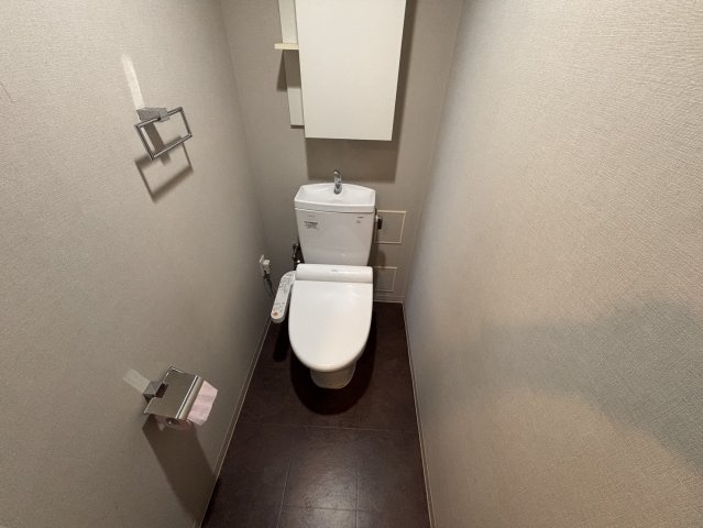 清潔感のあるシンプルなトイレ空間。温水洗浄便座や手洗い洗面、トイレットペーパーなどをすっきり収納できる上部吊戸棚を備えており、衛生面と機能性の両方に配慮されています。
