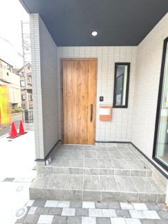 【玄関】 | 廿日市市阿品2丁目（阿品駅）新築未入居 | 屋根付きのポーチは雨の日の出入りもスムーズ。木目調の玄関ドアとタイルの質感が温かみのあるアプローチを演出しています。