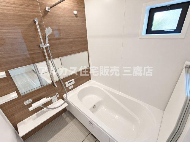 調布市東つつじケ丘2丁目 新築戸建 京王線 つつじヶ丘駅 の浴室|木目調パネルが温かみを演出するバスルーム。ゆったり寛げる浴槽と換気に便利な小窓を備えています。
