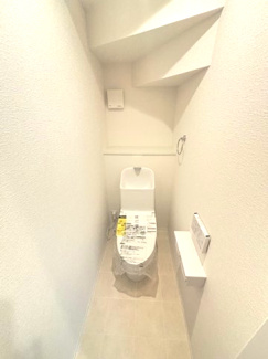 【トイレ】 | 東広島市西条町御薗宇　NO10【57坪】 | 階段下のスペースを有効活用した1階の温水洗浄便座付きトイレ。スッキリとしたデザインの便器を採用しており、ペーパーホルダーやタオル掛け、小物を置ける便利なカウンター棚も完備しています。