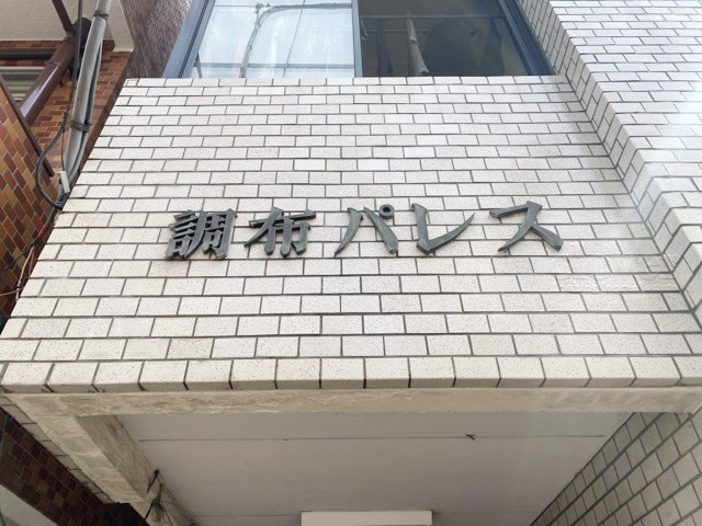 【現況写真】 | 調布パレス | エントランスに掲げられた、マンション名を示す館銘板。さほど激しく主張はしませんが、しっかりと掲示されています。～即日のご見学可能～　お問合せはお気軽にどうぞ。